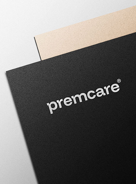 Neues Logo von premcare® in Weiß, geprägt auf schwarzem Papier mit braunem Hintergrund