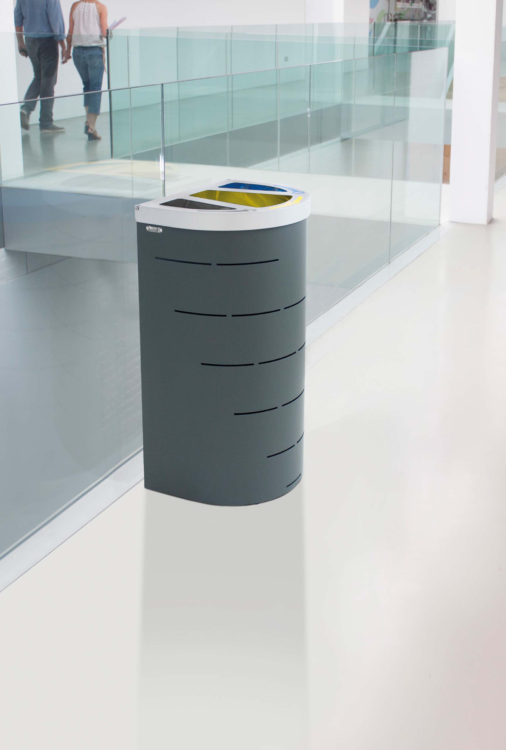 „Modernes Recycling‑ und Abfalltrennsystem mit drei farblich markierten Einwurföffnungen neben einer Glasbrüstung in einem hellen, minimalistischen Innenraum.